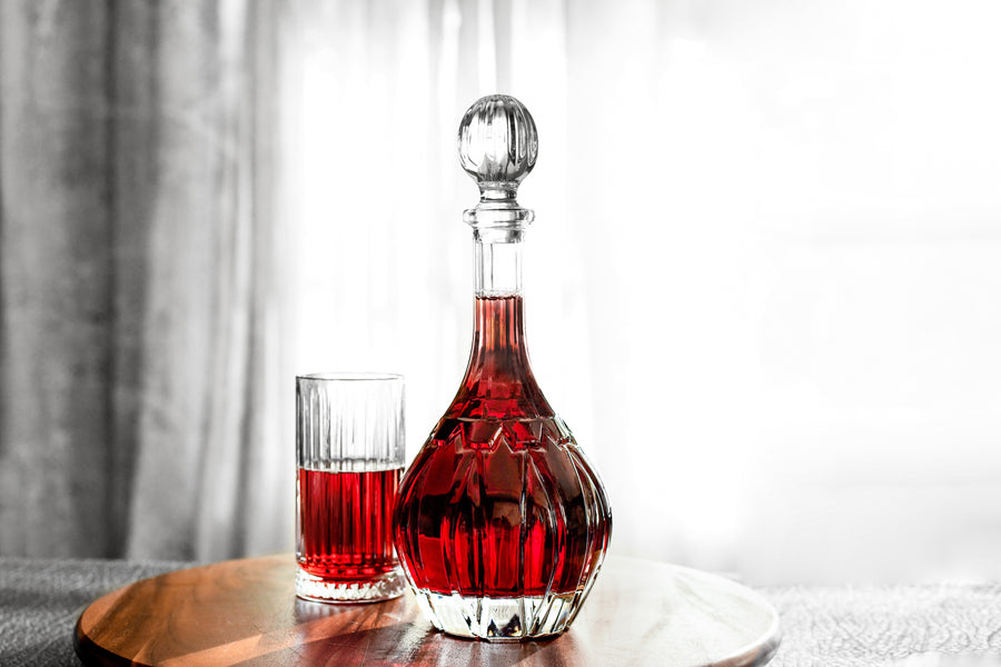 Bordeaux 34 oz crystal-cut wine decanter with ball stopper, filled with red wine beside two ribbed glasses